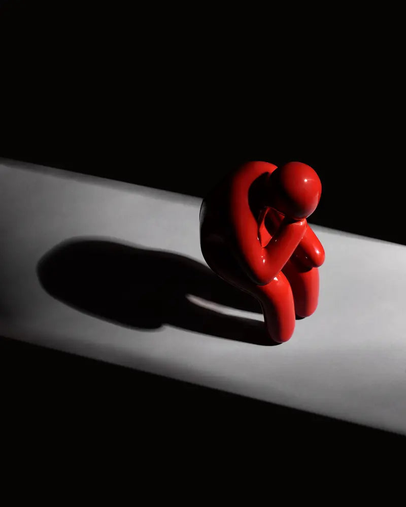 Sobrepensante rojo sentado al borde de un pedestal blanco, con su sombra